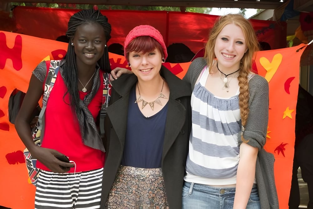 Drei junge Schülerinnen stehen vor einem farbenfrohen Herz-Motiv auf dem Cyril Jackson Senior Campus.