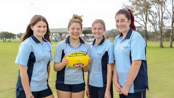 Vier Schülerinnen des Dalyellup College stehen gemeinsam auf einem Rasenfeld und halten einen Australian Rules Football.