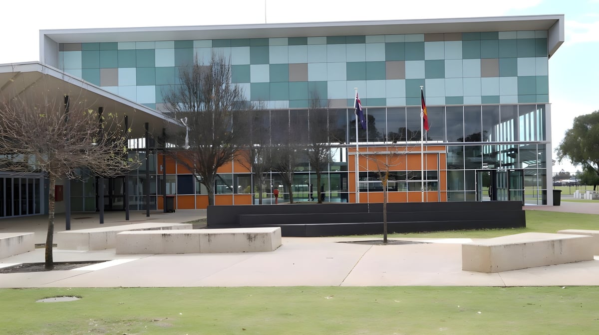 Das moderne Glas- und Stahlgebäude von Dalyellup College steht vor einem grasbewachsenen Bereich mit Bänken und Treppen.