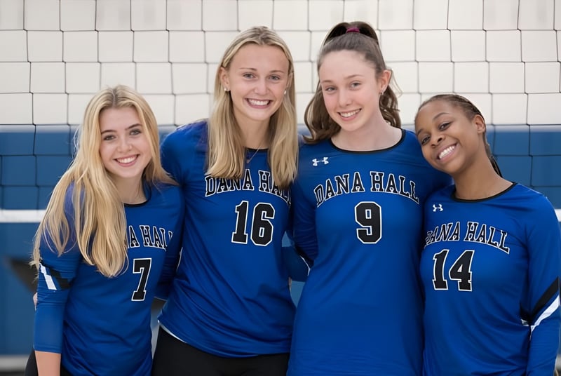 Vier Schülerinnen der Dana Hall School stehen in Volleyballuniformen in der Turnhalle vor einem Volleyballnetz.