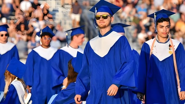 Eine Gruppe von Absolventen in blauen Talaren der Daniel McIntyre Collegiate Institute geht gemeinsam bei einer Abschlussfeier.