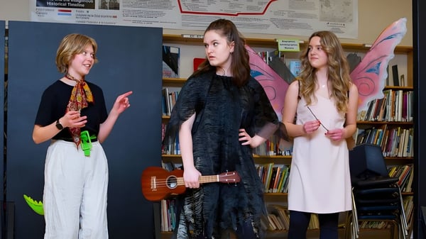 Drei Schülerinnen des Daniel McIntyre Collegiate Institute stehen mit einer Ukulele in einem Raum mit Bücherregalen.