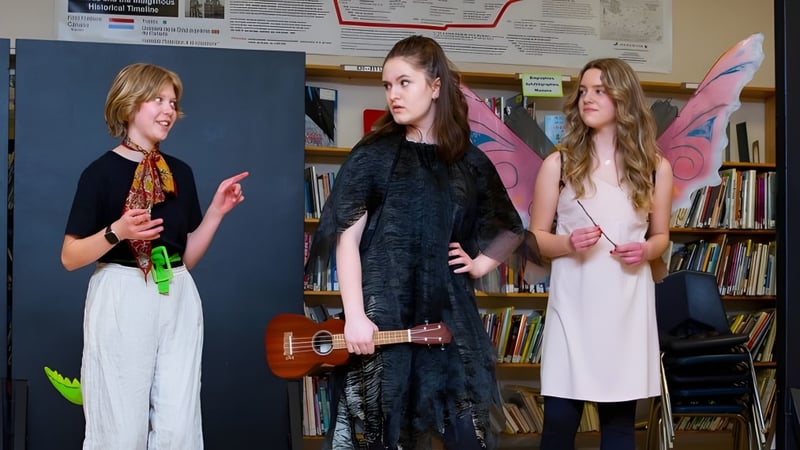 Drei Schülerinnen des Daniel McIntyre Collegiate Institute stehen mit einer Ukulele in einem Raum mit Bücherregalen.