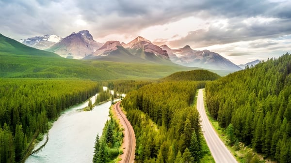 Ein gewundener Feldweg führt durch eine grüne Wiese mit schneebedeckten Bergen im Hintergrund auf dem Gelände des Daniel McIntyre Collegiate Institute.