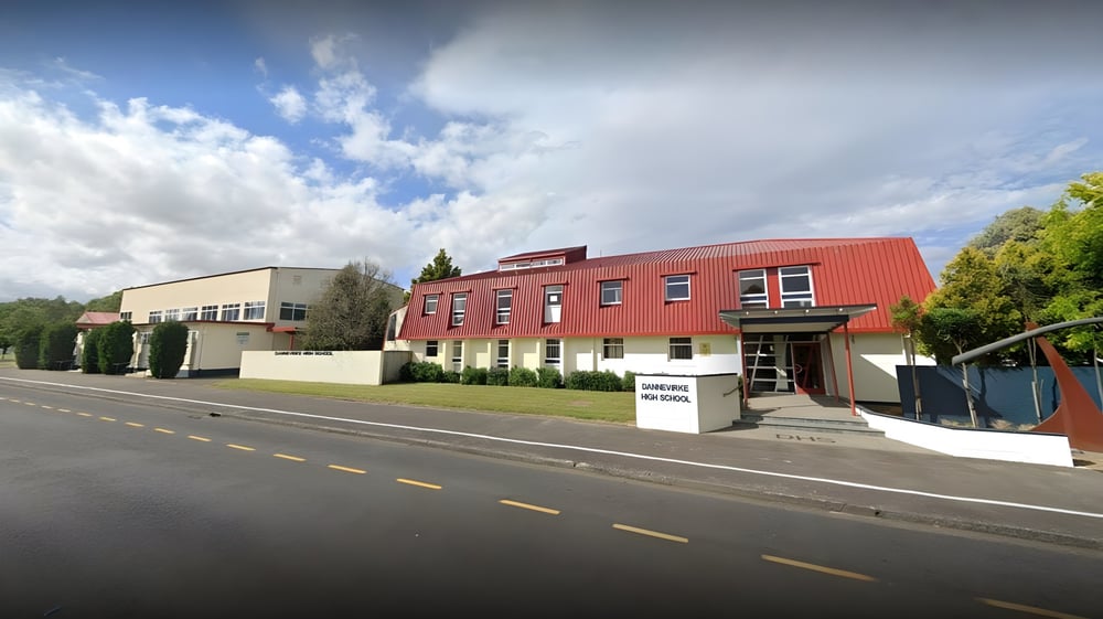 Das moderne mehrstöckige Gebäude der Dannevirke High School mit roter Fassade steht an einer Straße und ist von Bäumen umgeben.