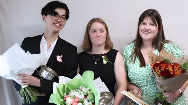 Drei Personen halten bei einer Feier auf dem Campus der Darfield High School Blumensträuße.