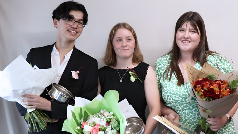 Drei Personen halten bei einer Feier auf dem Campus der Darfield High School Blumensträuße.