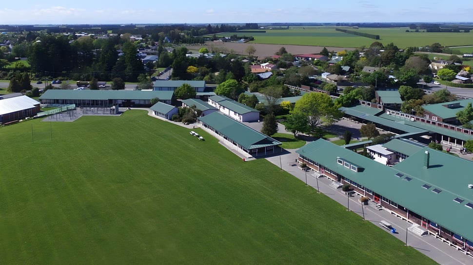 Landschaft mit grünen Feldern und Gebäuden vor bewaldeten Hügeln auf dem Gelände der Darfield High School.