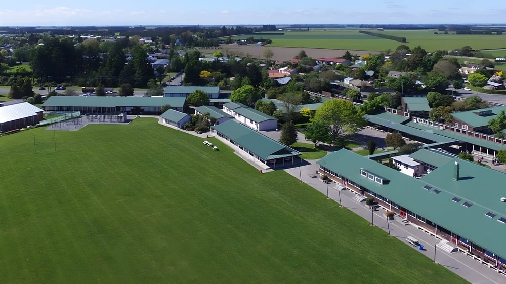 Landschaft mit grünen Feldern und Gebäuden vor bewaldeten Hügeln auf dem Gelände der Darfield High School.