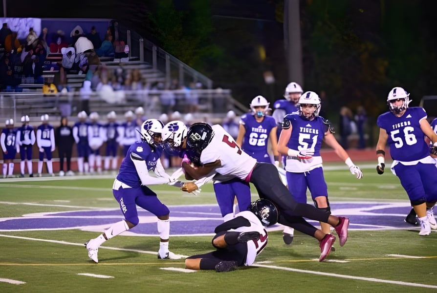 Fußballspiel mit Spielern im Tackling auf dem Spielfeld der Darlington School vor Zuschauern.