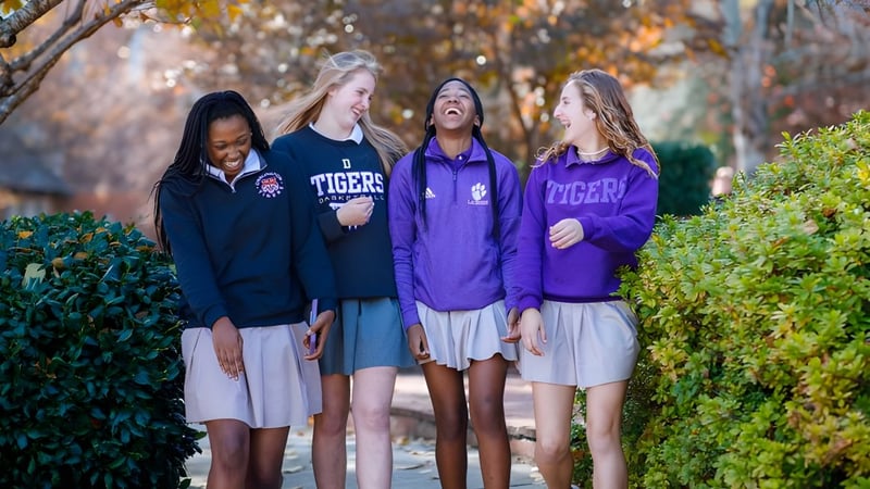 Vier Schülerinnen der Darlington School stehen zusammen im Freien vor Bäumen und Laub.