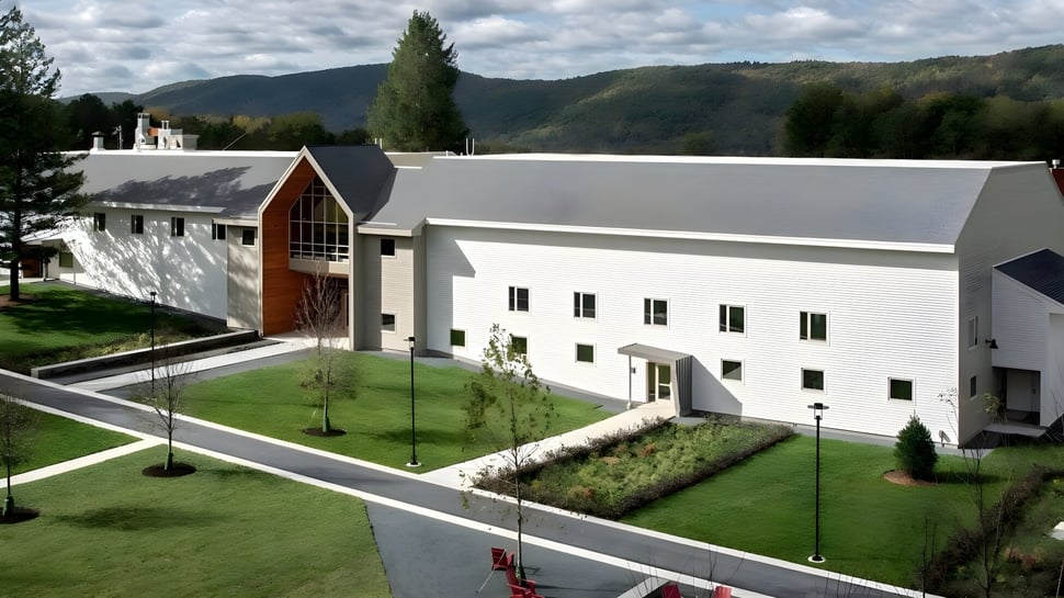 Das moderne weiße Gebäude der Darrow School mit markantem Bogen im gepflegten Umfeld und grünen Hügeln im Hintergrund.