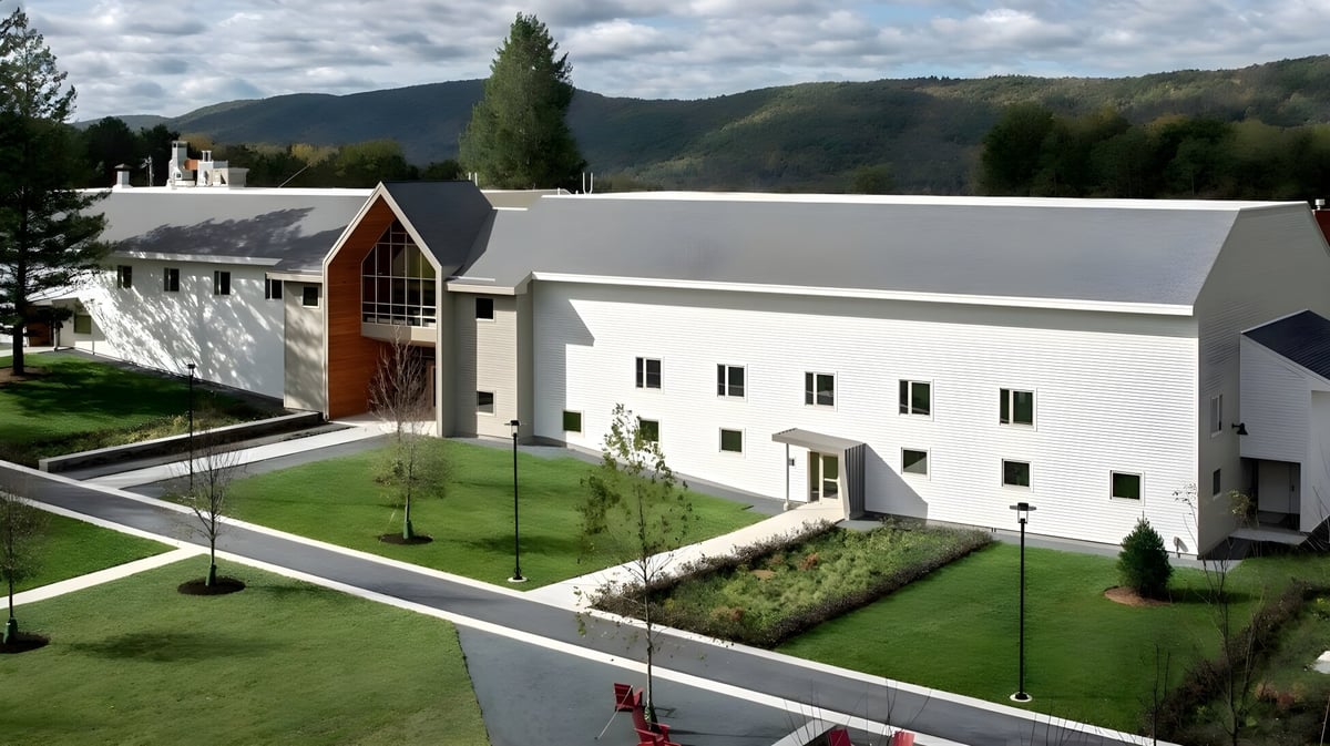 Das moderne weiße Gebäude der Darrow School mit markantem Bogen im gepflegten Umfeld und grünen Hügeln im Hintergrund.