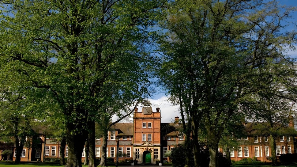 Historisches Backsteingebäude der Dauntsey’s School umgeben von grünen Bäumen unter blauem Himmel.