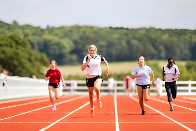 Eine Gruppe von Läuferinnen sprintet auf der Laufbahn auf dem Sportgelände der Dauntsey’s School vor bewaldetem Hintergrund.