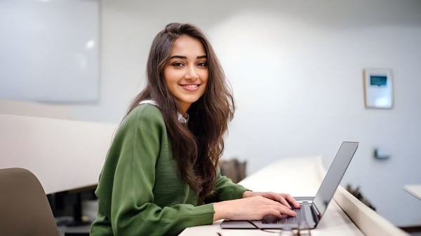 Eine junge Frau sitzt am Schreibtisch und nutzt im Arbeitsbereich am David Game College Liverpool einen Laptop.