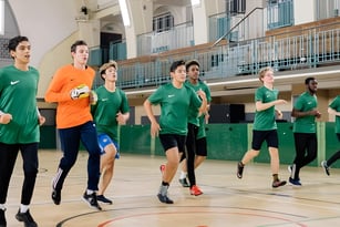 Eine Gruppe von Schülern des David Game College Liverpool läuft gemeinsam in der Sporthalle mit Basketballfeld und Tribünen.