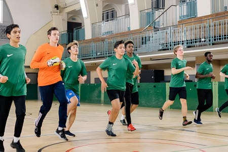 Eine Gruppe von Schülern des David Game College Liverpool läuft gemeinsam in der Sporthalle mit Basketballfeld und Tribünen.