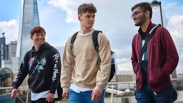Drei junge Männer stehen in urbaner Umgebung mit Stadtblick auf dem Campus des David Game College Liverpool.