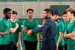Eine Gruppe Schüler des David Game College diskutiert im Sportzentrum mit ihrem Trainer eine Teamstrategie.