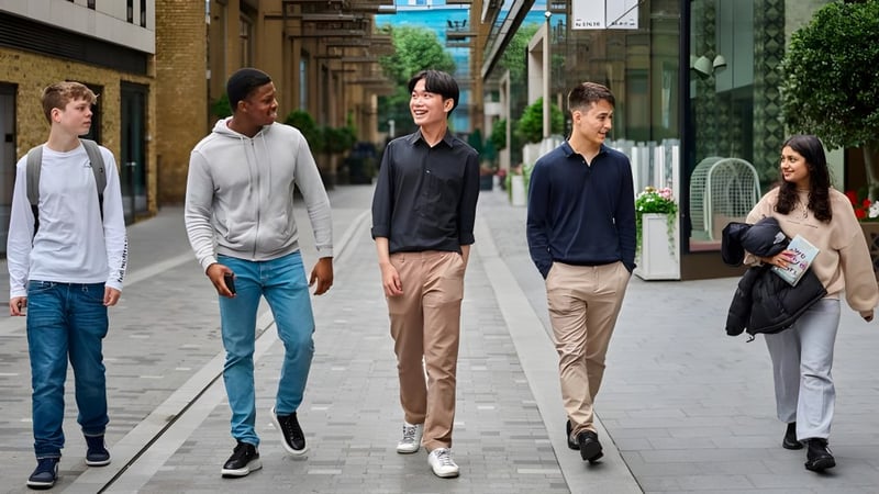 Eine Gruppe Schülerinnen und Schüler des David Game College geht zusammen eine Straße mit Gebäuden und Geschäften entlang.