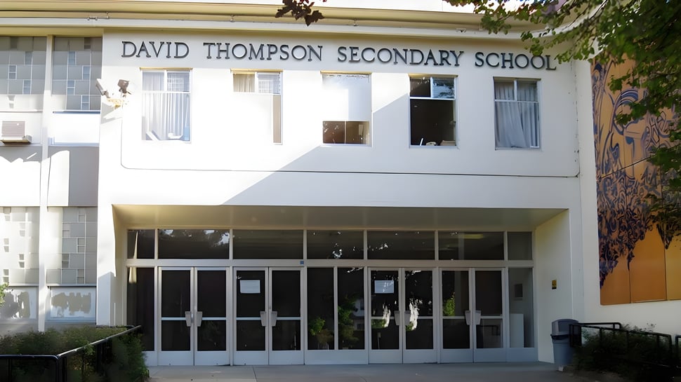 Das Gebäude der David Thompson Secondary School mit einem gläsernen Eingang und einem Baum im Vordergrund.