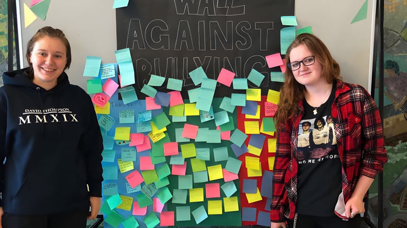 Zwei Schülerinnen stehen vor der Anti-Bullying-Wand mit bunten Notizen an der David Thompson Secondary School.