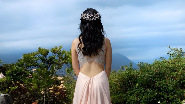 Person mit langem dunklem Haar in rosa Kleid steht in einer grünen Landschaft vor Bergen auf dem Gelände der David Thompson Secondary School.