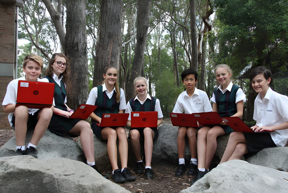 Schüler der Davidson High School sitzen in Schuluniformen auf Felsen in einer bewaldeten Umgebung.