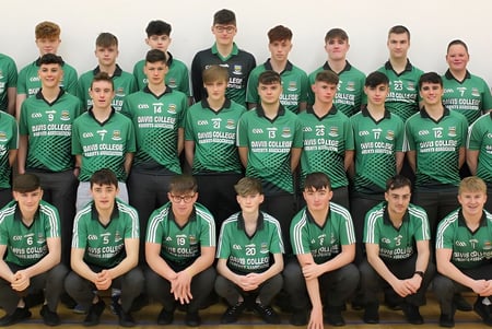 Eine Gruppe junger Athleten in grünen Trikots posiert auf dem Campus des Davis College vor weißem Hintergrund.