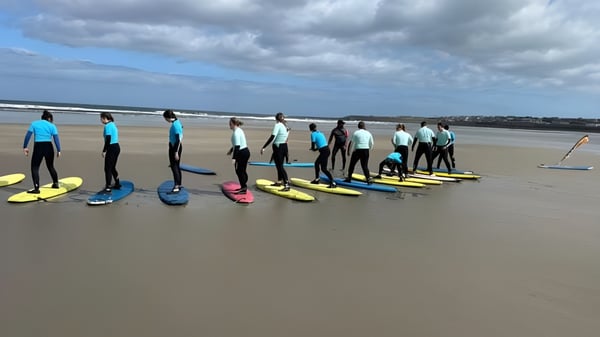 Schüler des Davitt College nehmen am Surfkurs am Strand bei bewölktem Himmel teil.