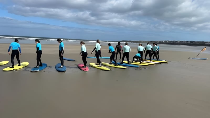 Schüler des Davitt College nehmen am Surfkurs am Strand bei bewölktem Himmel teil.