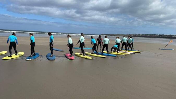 Schüler des Davitt College nehmen an einem Surfkurs am Strand bei bewölktem Himmel teil.