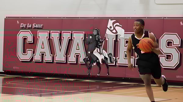 Ein Sportler steht auf dem Basketballfeld mit einem großen De La Salle Cavaliers Wandbild im Hintergrund auf dem Campus der École secondaire publique De La Salle.