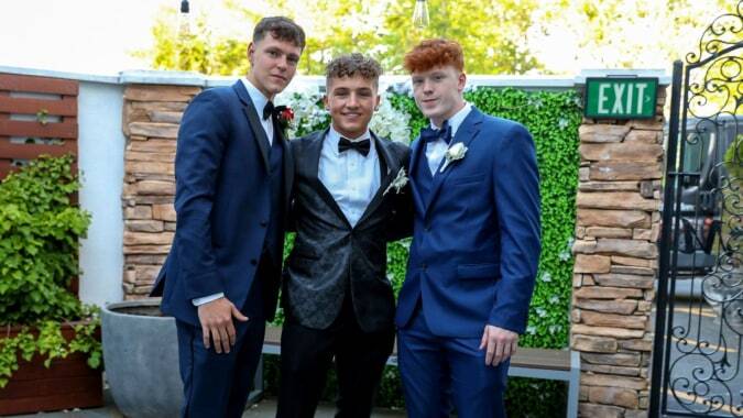 Drei Schüler des De la Salle College Churchtown in formeller Kleidung stehen vor einer Steinmauer im Freien.