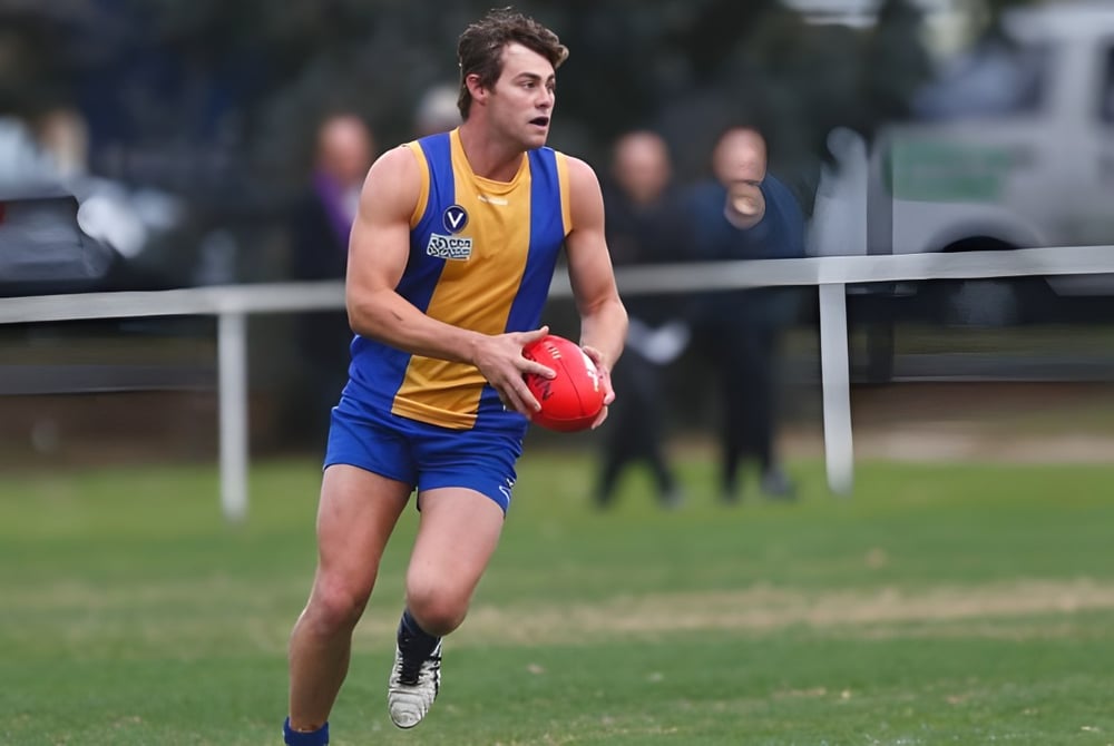 Ein junger Athlet in blau-gelber Uniform läuft mit einem roten Football auf dem Spielfeld des De la Salle College Churchtown.