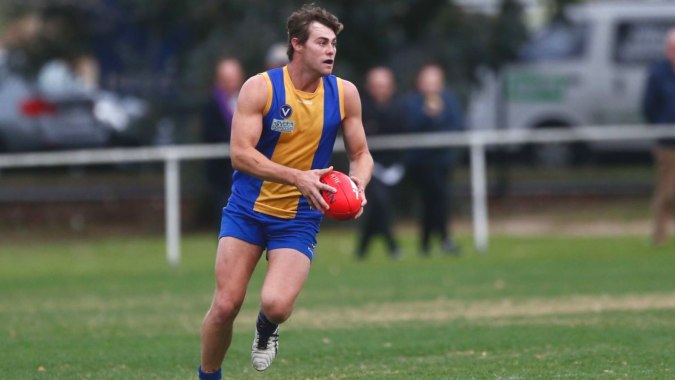 Ein Schüler des De la Salle College (Churchtown) läuft mit einem roten Football auf einem Grasfeld.
