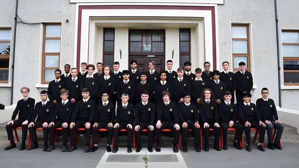 Eine Gruppe Schüler des De la Salle College Churchtown steht in formeller Schuluniform vor einem prachtvollen Gebäude.