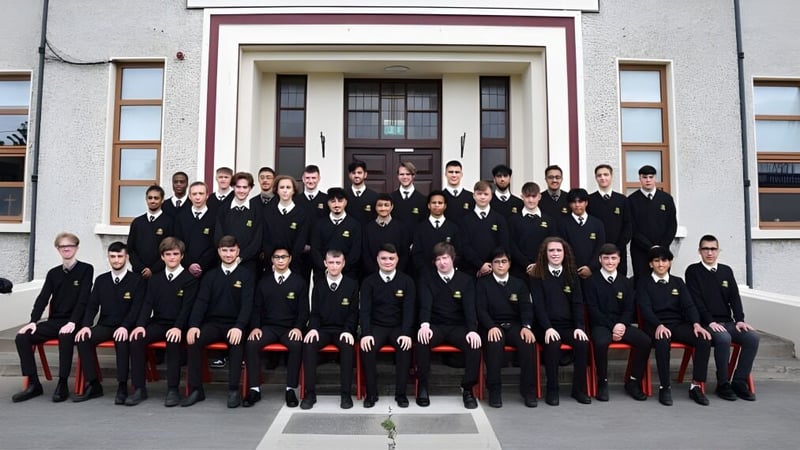 Eine Gruppe Schüler des De la Salle College Churchtown steht in formeller Schuluniform vor einem prachtvollen Gebäude.