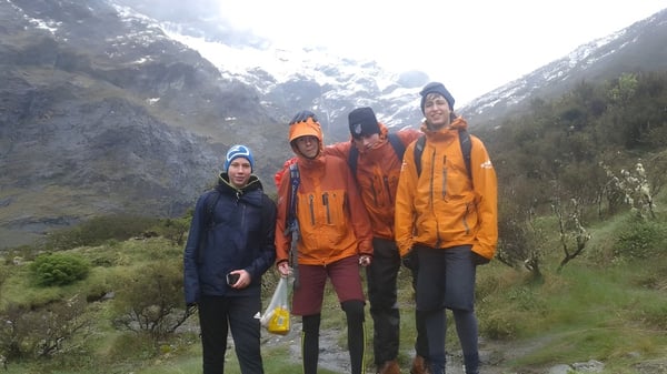 Eine Gruppe Schülerinnen und Schüler des De la Salle College Macroom steht bei einer Wanderung in bunter Regenkleidung in einer bergigen Landschaft mit schneebedeckten Gipfeln.