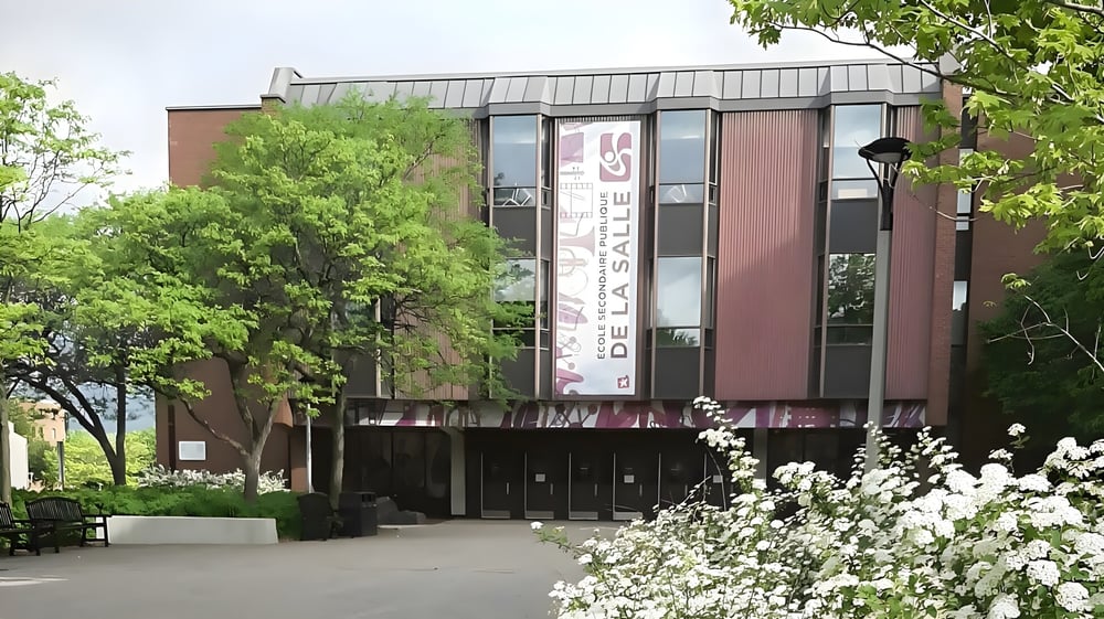 Das moderne Backsteingebäude mit Glasfassade der École secondaire publique De La Salle steht umgeben von grünem Bewuchs und weißen Blüten.
