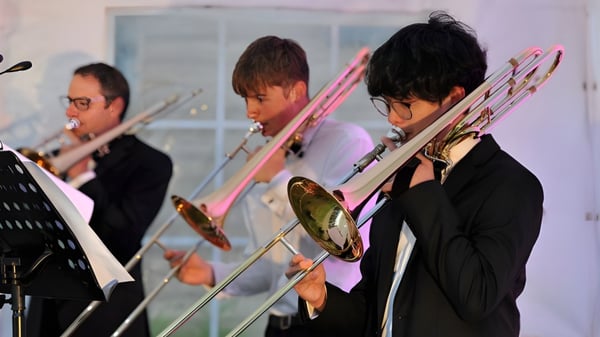 Schüler der Dean Close School spielen verschiedene Blechblasinstrumente auf einer Bühne während einer Aufführung.