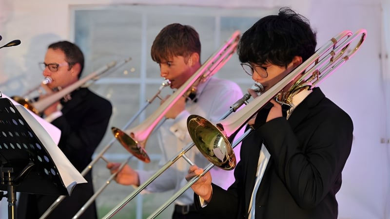 Schüler der Dean Close School spielen verschiedene Blechblasinstrumente auf einer Bühne während einer Aufführung.