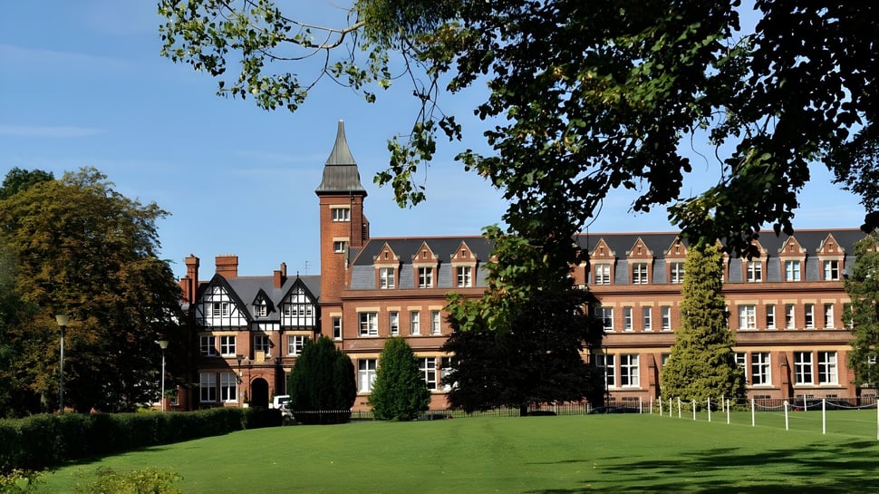Das historische Backsteingebäude auf dem grünen Campus der Dean Close School mit gepflegtem Rasen im Vordergrund.