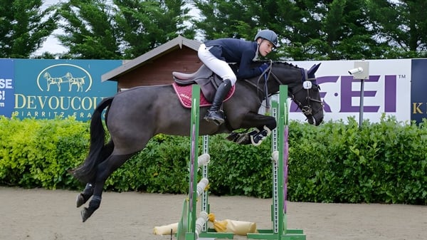 Eine Schülerin der Dean Close School reitet bei einem Pferdesprungwettbewerb vor grünen Bäumen.