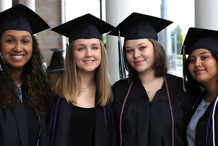 Vier Absolventinnen in Talar und Hut feiern ihren Abschluss vor einem Fenster auf dem Campus der Deer Valley Unified.