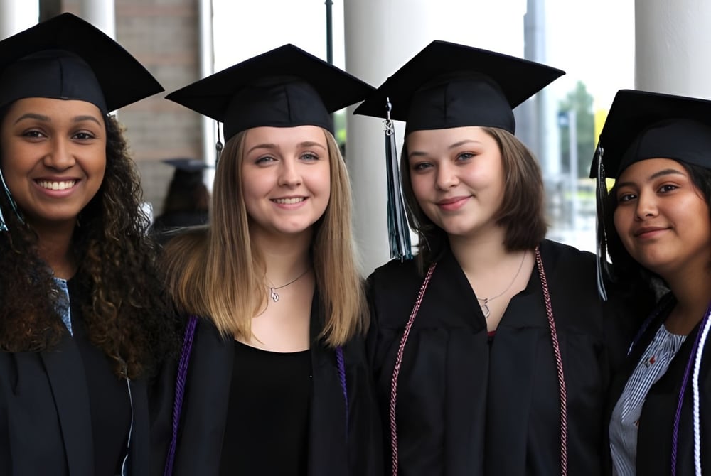 Vier Absolventinnen in Talar und Hut feiern ihren Abschluss vor einem Fenster auf dem Campus der Deer Valley Unified.