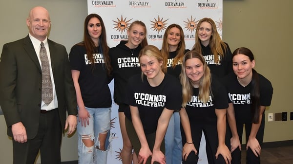 Eine Gruppe junger Frauen der Deer Valley Unified School trägt einheitliche T-Shirts mit O'Connor Volleyball vor einem Deep Valley Logo.
