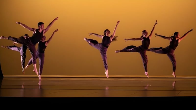 Eine Gruppe Tänzerinnen und Tänzer der Deerfield Academy führt eine synchronisierte Performance auf der Bühne vor einem goldfarbenen Hintergrund auf.