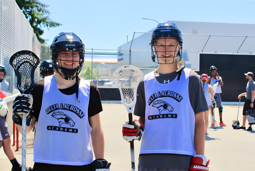 Zwei Schülerinnen der Delta Secondary School tragen Lacrosse-Uniformen und stehen auf einem Sportfeld.